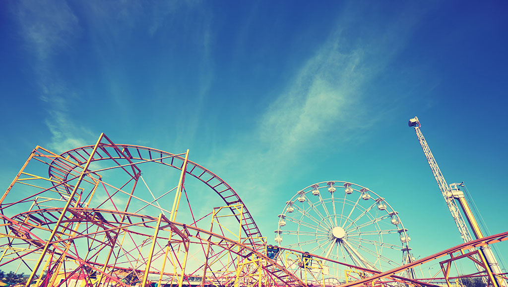 Amusement park setting with small roller coaster and ferris wheel against a blue sky in the background
