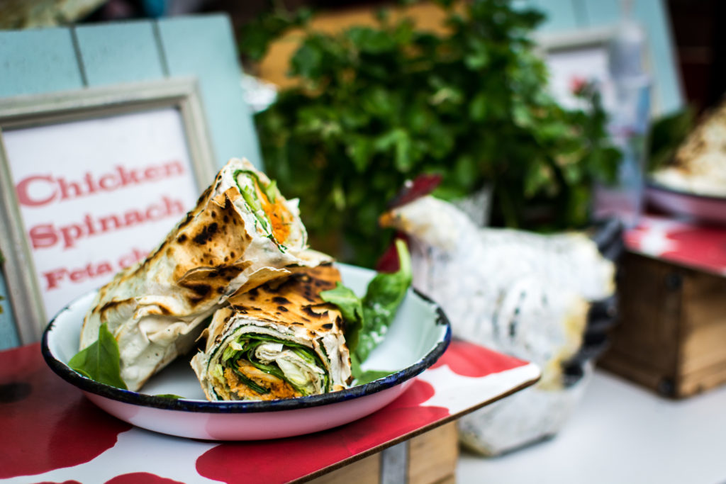 photo of a grilled wrap on a plate on display in front of a sign reading "chicken, spinach, feta cheese"