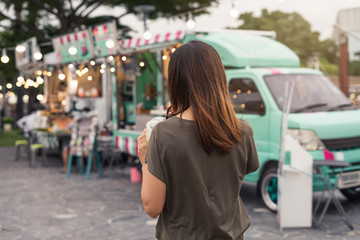 young woman walks by colorful food trucks with a smoothie in hand