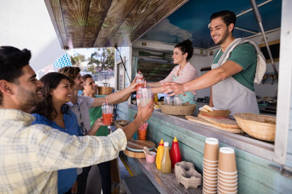 smiling food truck workers serve drinks to a group of young people