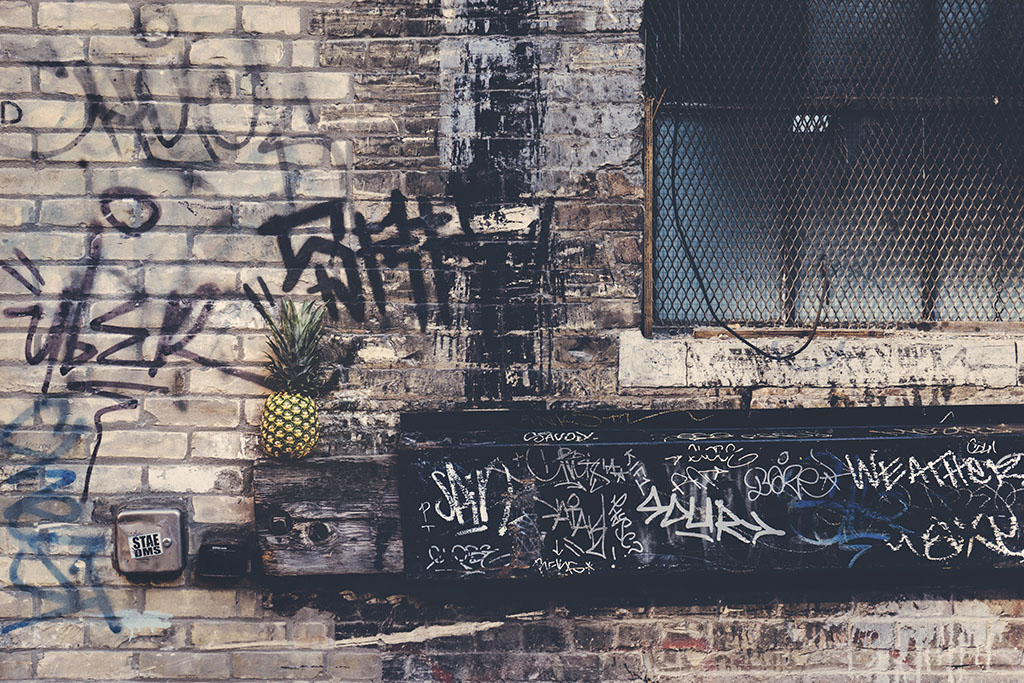 photo of a pineapple sitting on a ledge on the side of a graffitied urban building 