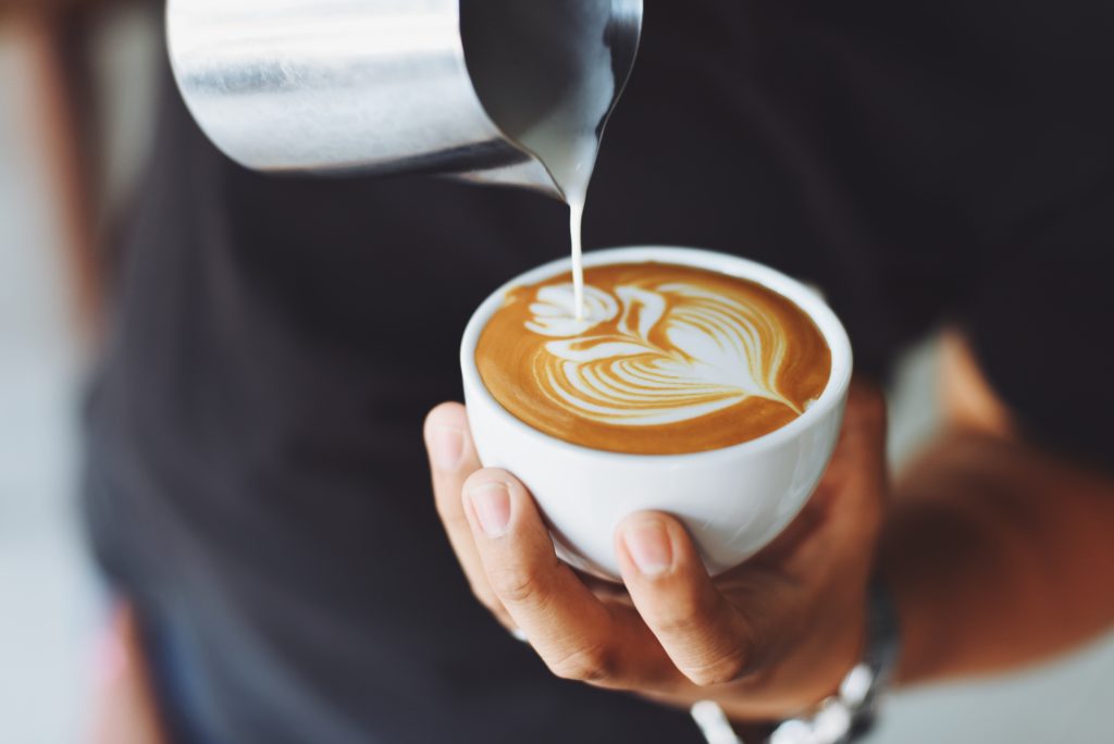 mobile coffee shop: close up of barista's hands as he pours milk into a swirling design atop a coffee drink in a mug