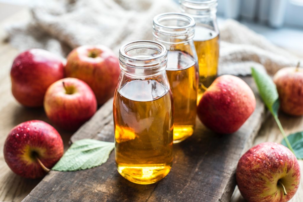 fall themed image with three jars of apple juice on a wooden board surrounded by apples