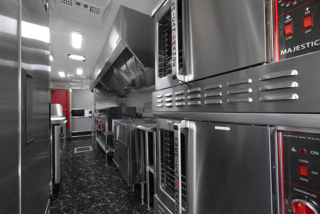 photo of a food truck interior showing ovens, stove, fryers, exhaust hood, proofing cabinet, refrigerator, and other kitchen equipment