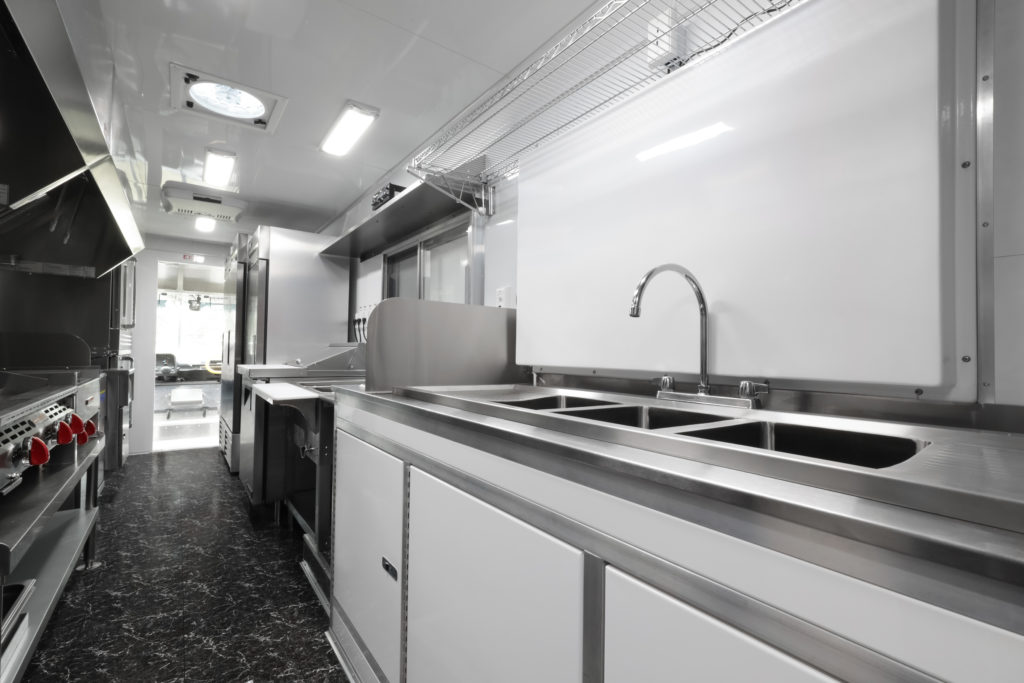 photo of a food truck interior showing a sanitation sink, stove, sandwich prep table, refrigerators and other appliances