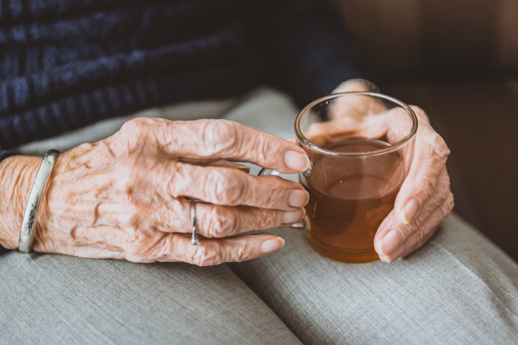 close up of old woman's hands holding a glass mug of tea on her lap