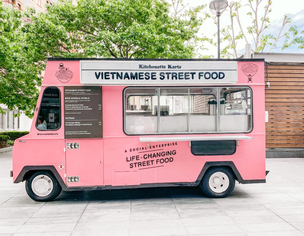 pink food truck selling Vietnamese street food parked in city square