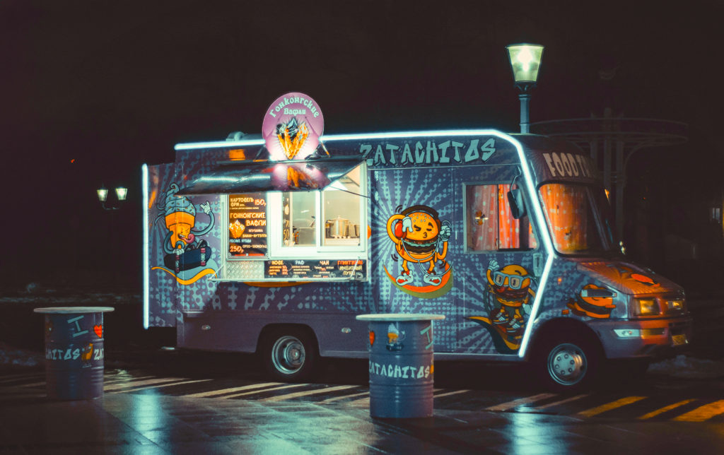 Photo of a blue burger food truck with neon lights parked under a streetlamp in a parking lot