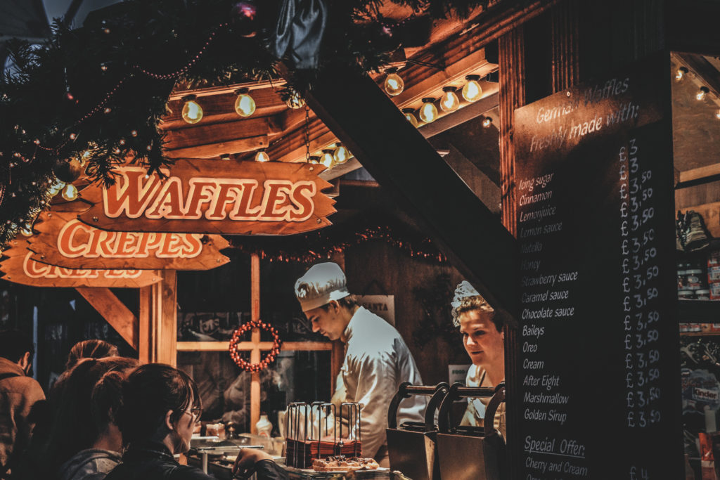 photo of male and female chefs selling from a food stall with signs for waffles and crepes
