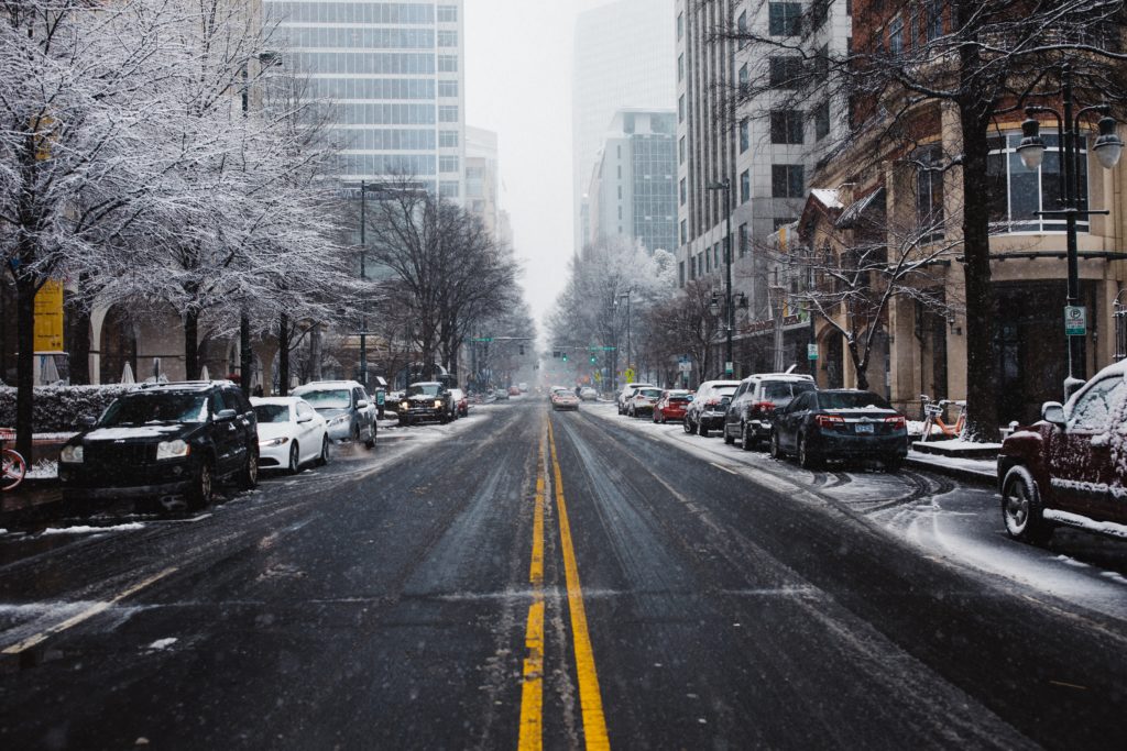 photo of a snowy urban street with trees, parked cars, and buildings