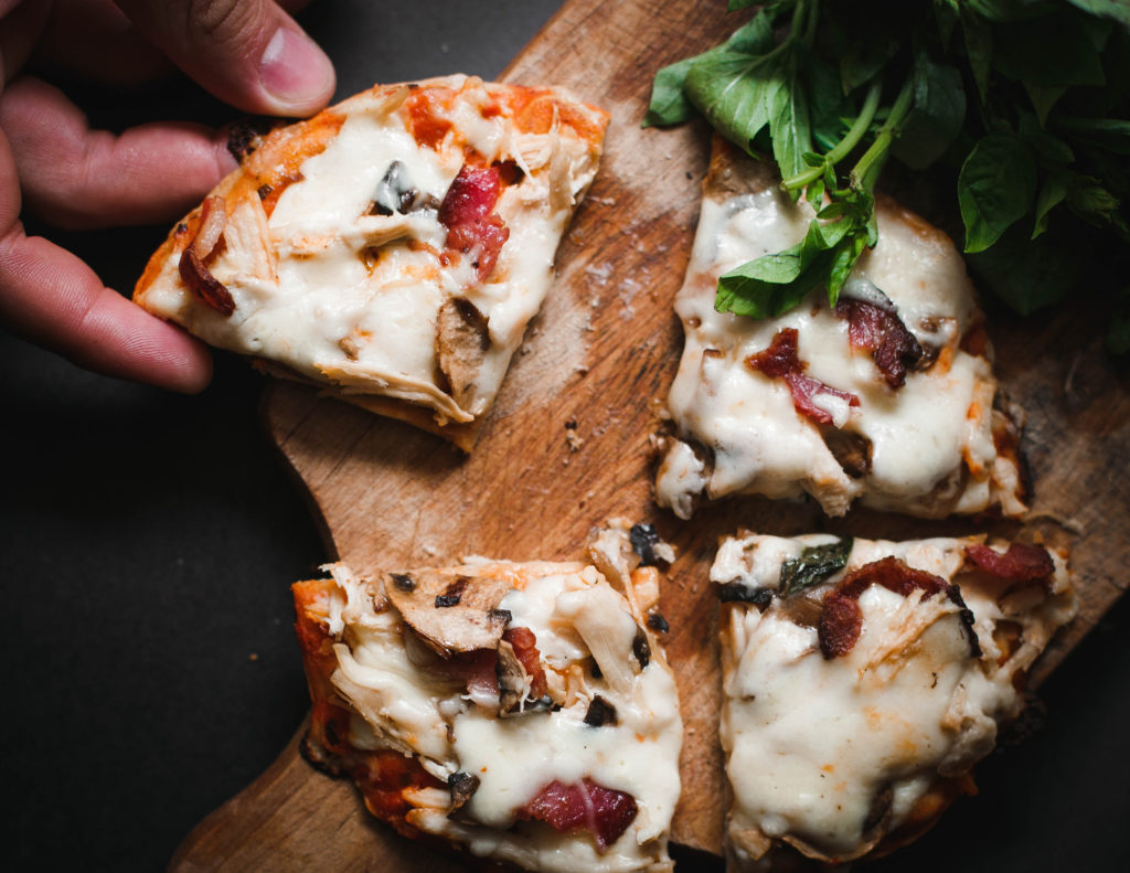 photo of a hand taking a piece from a personal sized pizza on a wooden serving board