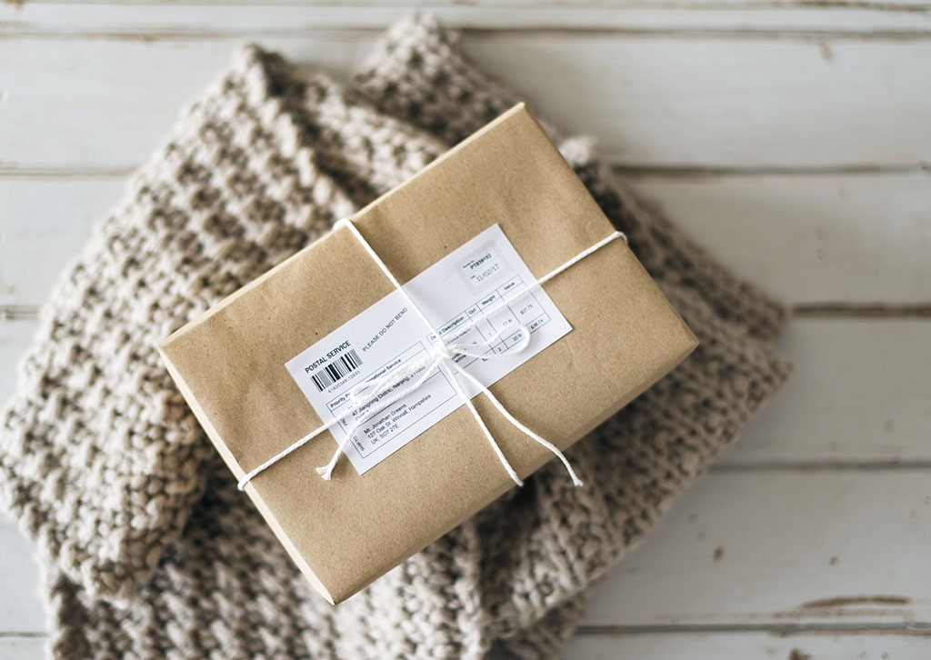 top down photo of a delivery package wrapped in brown paper and twin sitting on top of a knitted garment