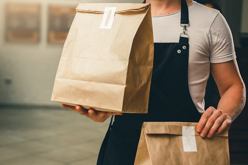 Two paper bags of delivery food being carried by a man in an apron