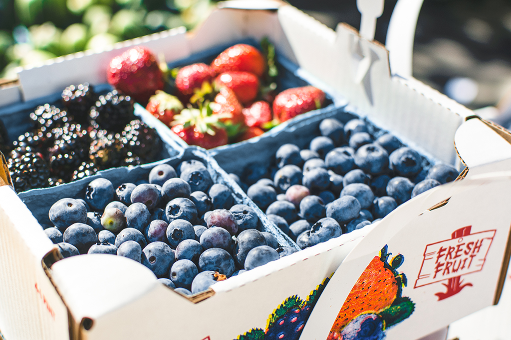 cartons of blueberries, blackberries and strawberries in a cardboard box at a farmer's market
