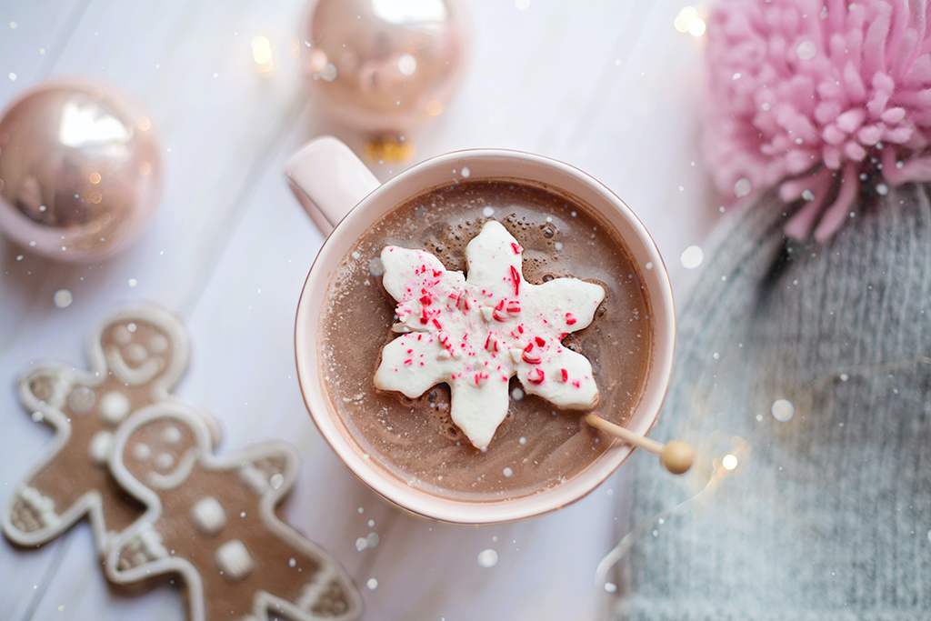 festive holiday photo of hot chocolate on a table with gingerbread, ornaments, and a winter hat